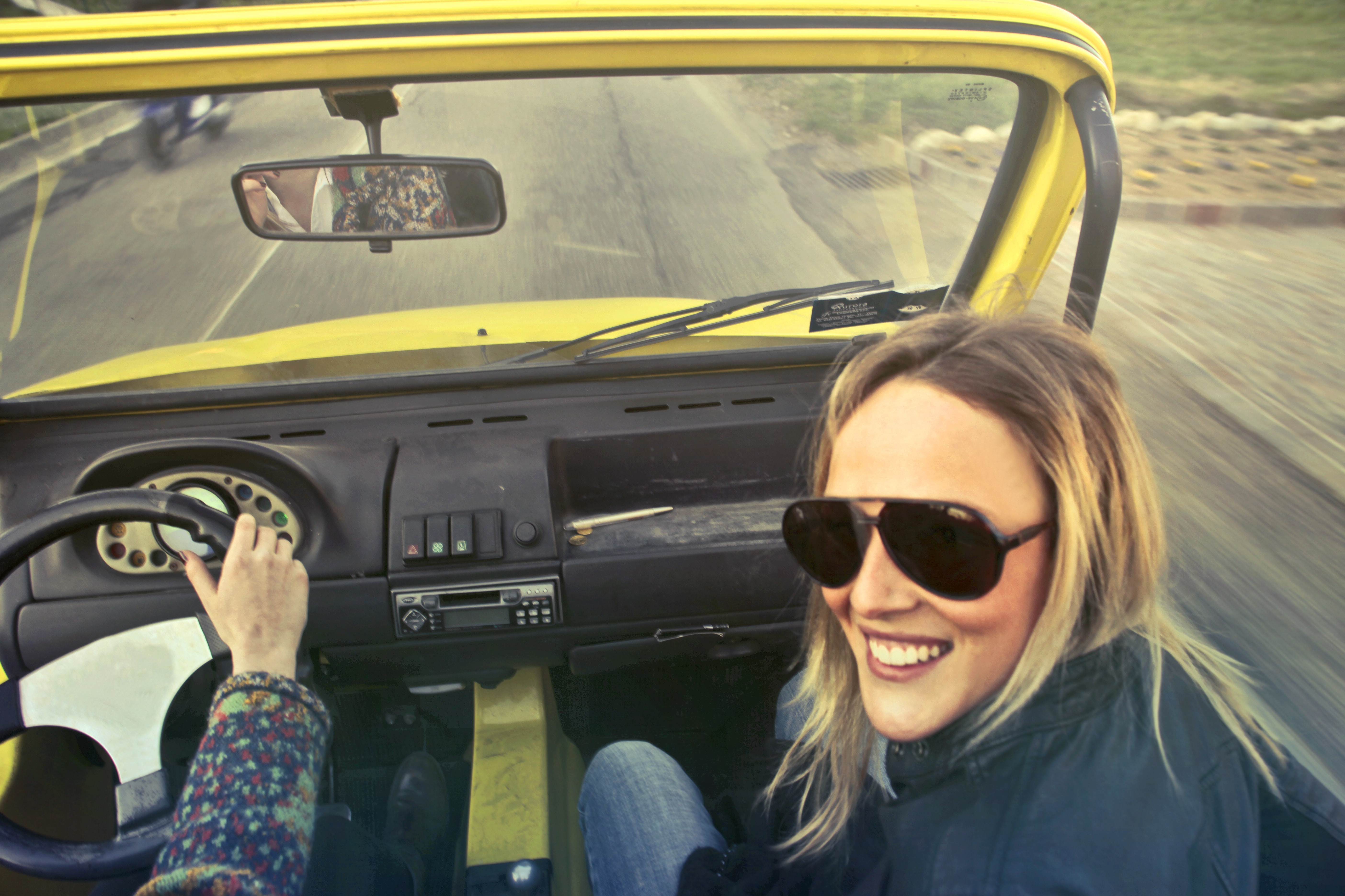 A woman with aviator glasses riding in a car looking toward the back seat.