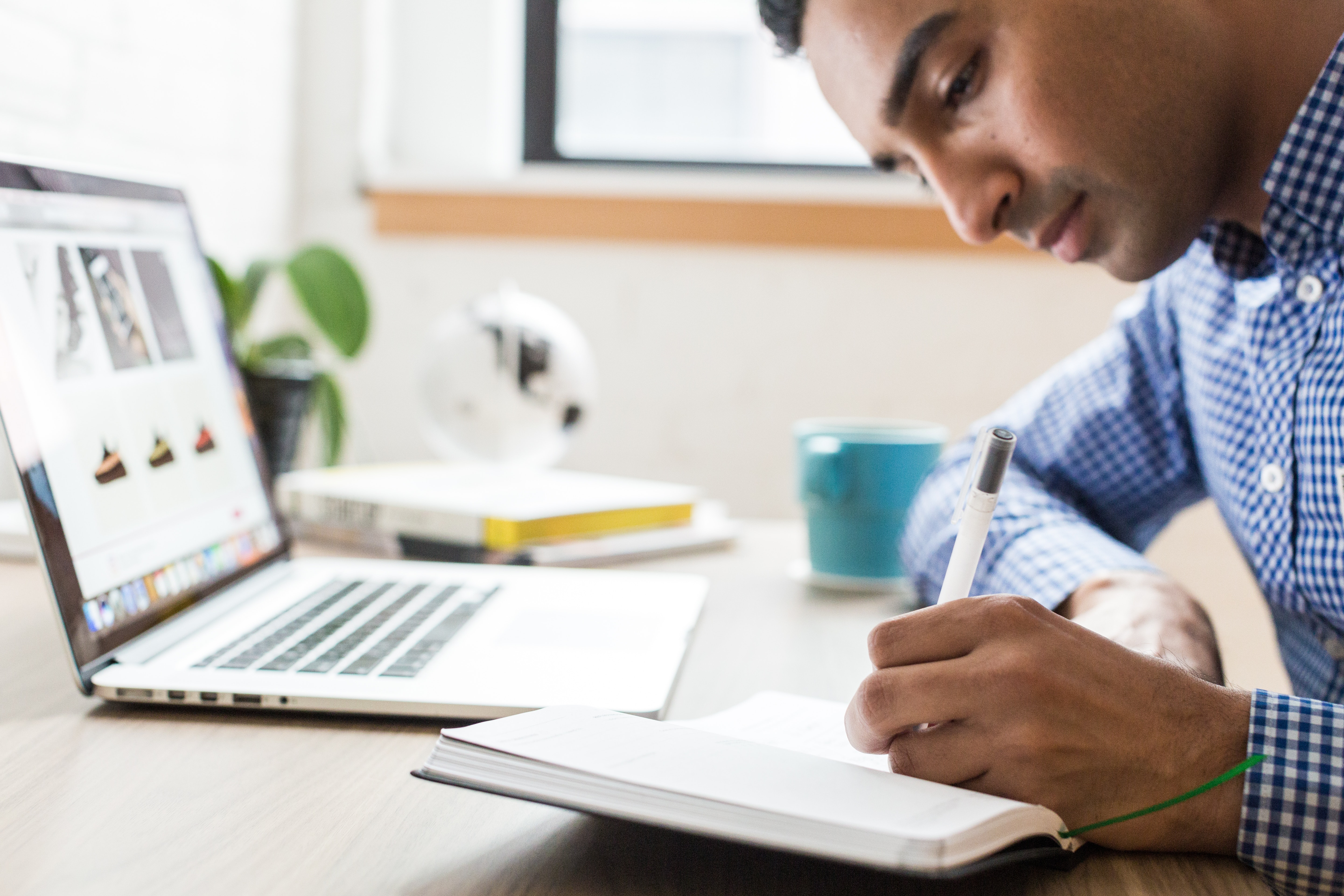 A man writing in a notebook with his laptop open