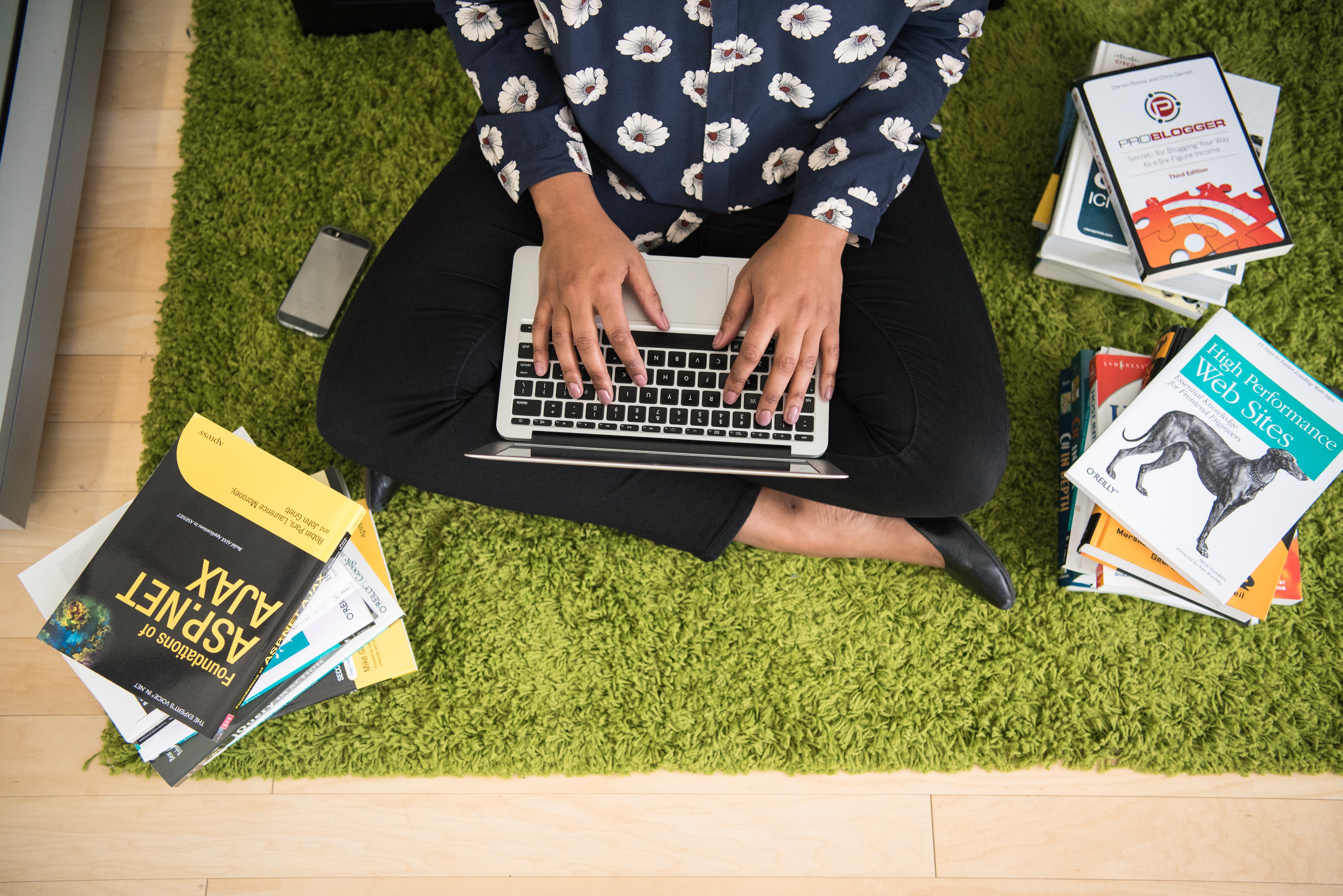 A woman surrounded by books typing on her laptop
