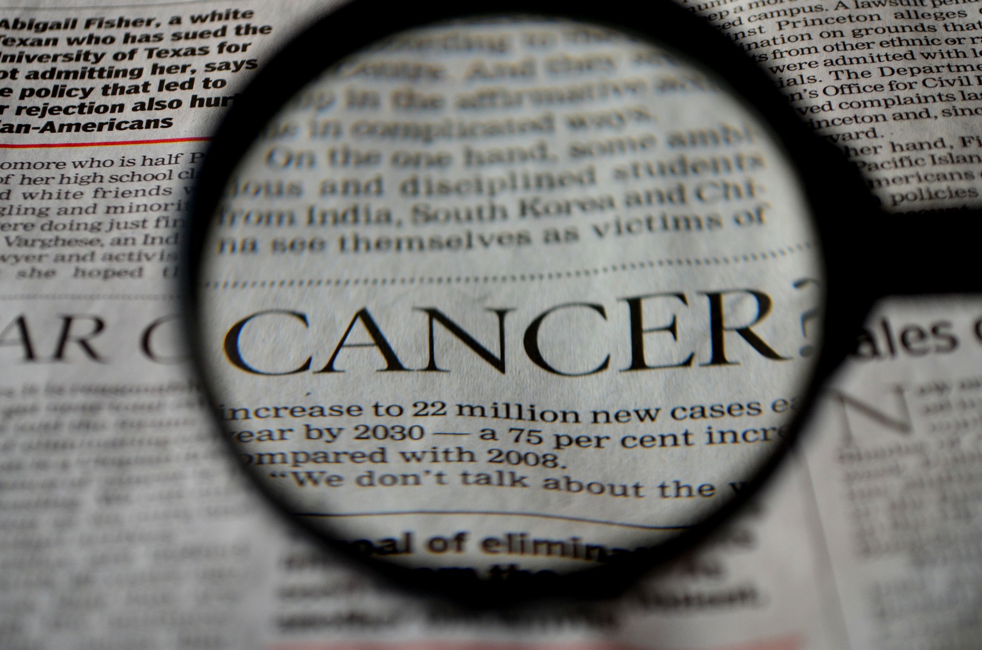 A magnifying glass focused on the word cancer in a newspaper