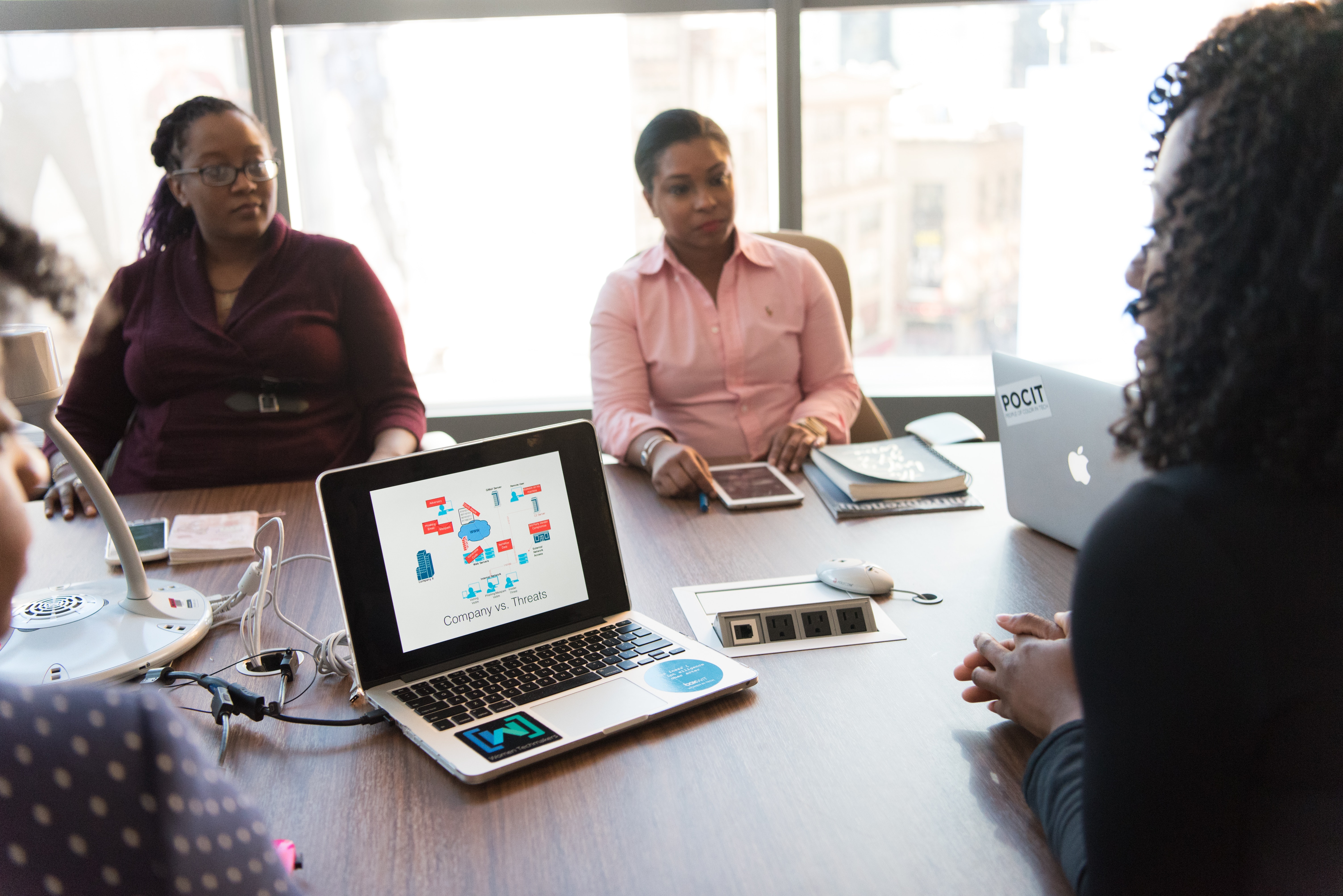 Women at a business meeting having a discussion with a PowerPoint presentation displayed on one computer.