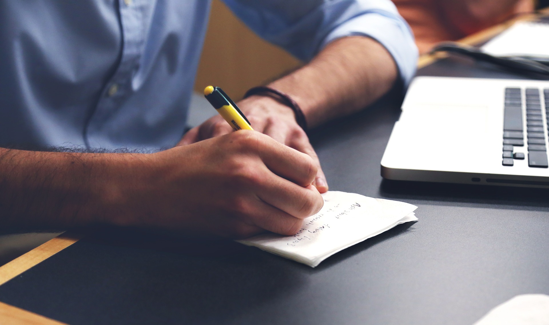 A person writing in a notebook with a computer nearby