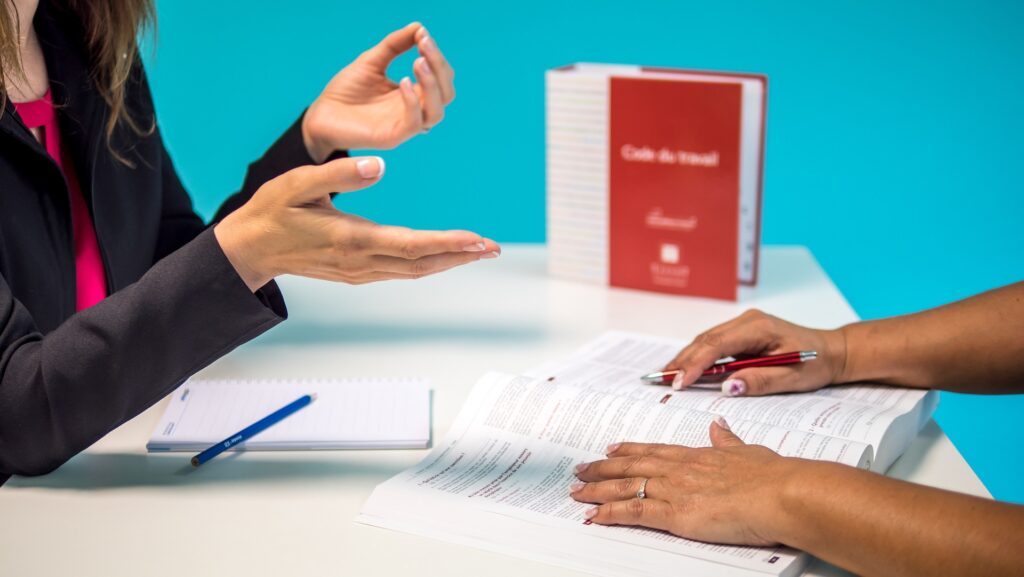 primer plano de las manos de dos mujeres sobre una mesa con papeles y un libro