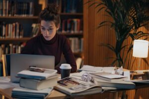 A woman surrounded by research writes a paper. 